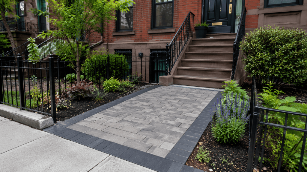 Paver walkway installation in Brooklyn at a brick row house, featuring a clean stone path bordered by greenery and designed to complement the home’s front entry.
