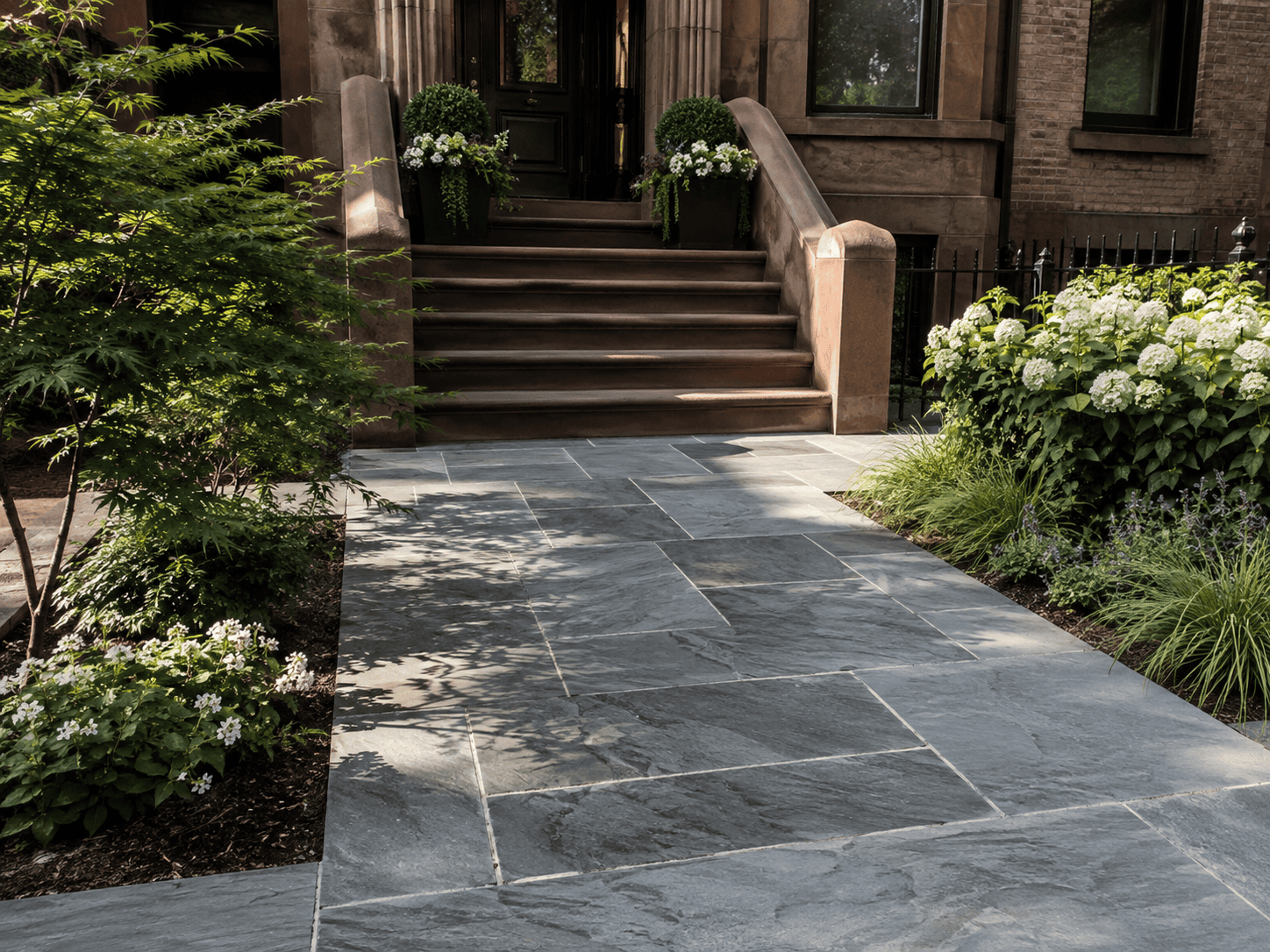Completed natural stone walkway with clean joints, landscaped edges and stone steps leading to a New York City brownstone entrance.